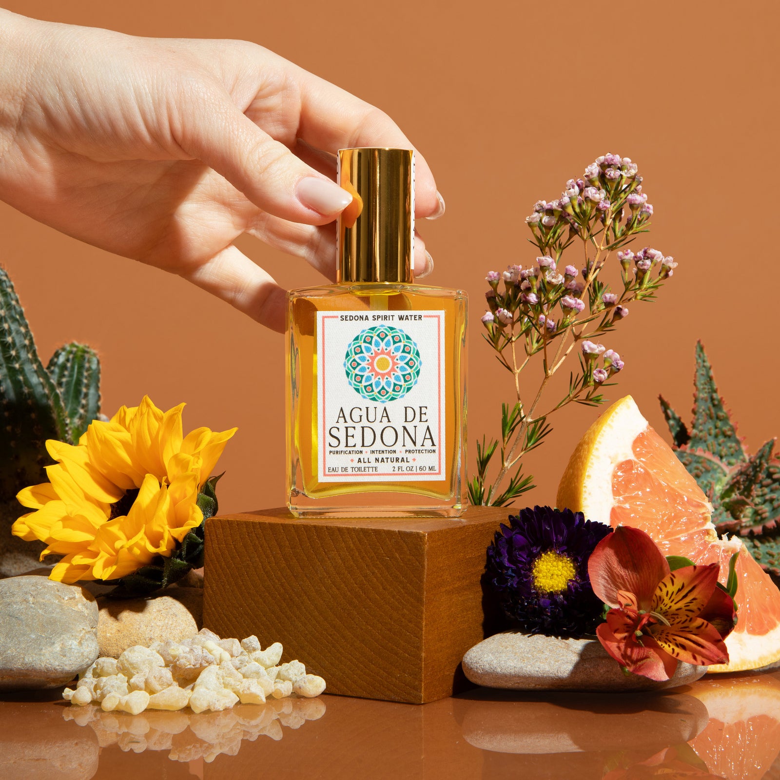 Agua de Sedona dropper bottle with flowers, grapefruit, and crystals on a warm brown backdrop