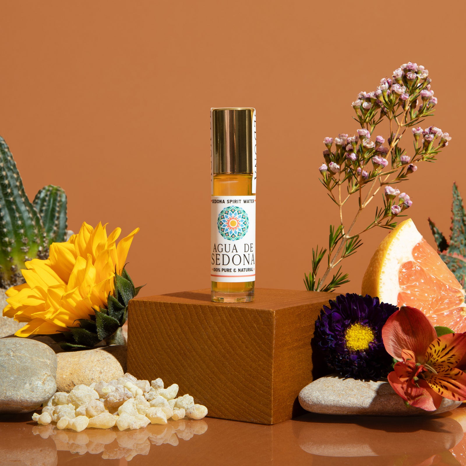 Agua de Sedona roll-on bottle with florals, citrus, and crystals on earthy background display.