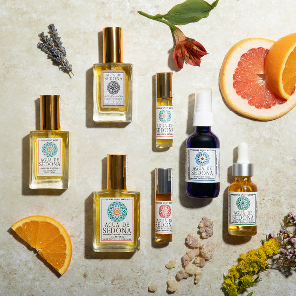 Flat lay of Agua de Sedona products with citrus slices, flowers, and crystals on a stone background.