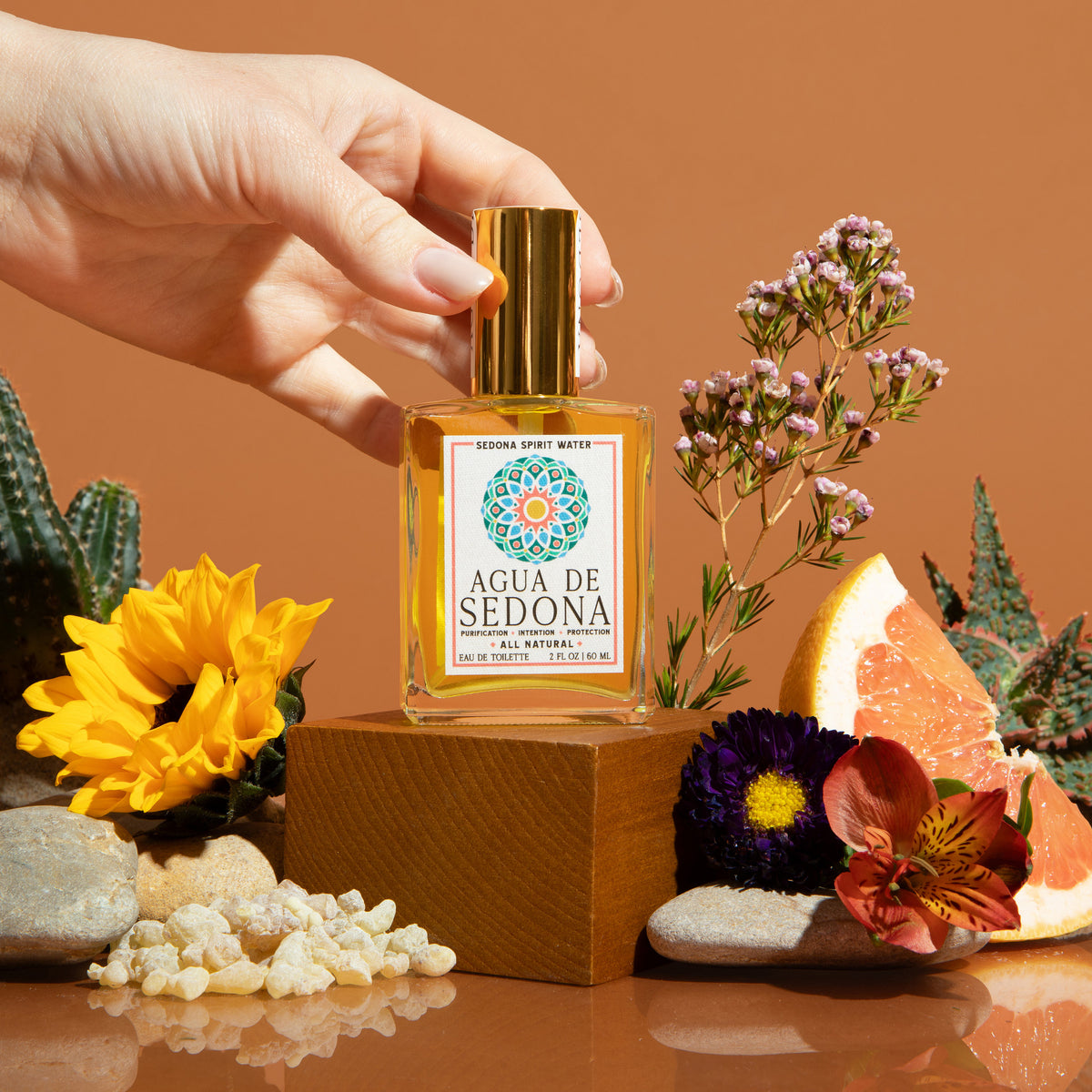 Agua de Sedona dropper bottle with flowers, grapefruit, and crystals on a warm brown backdrop