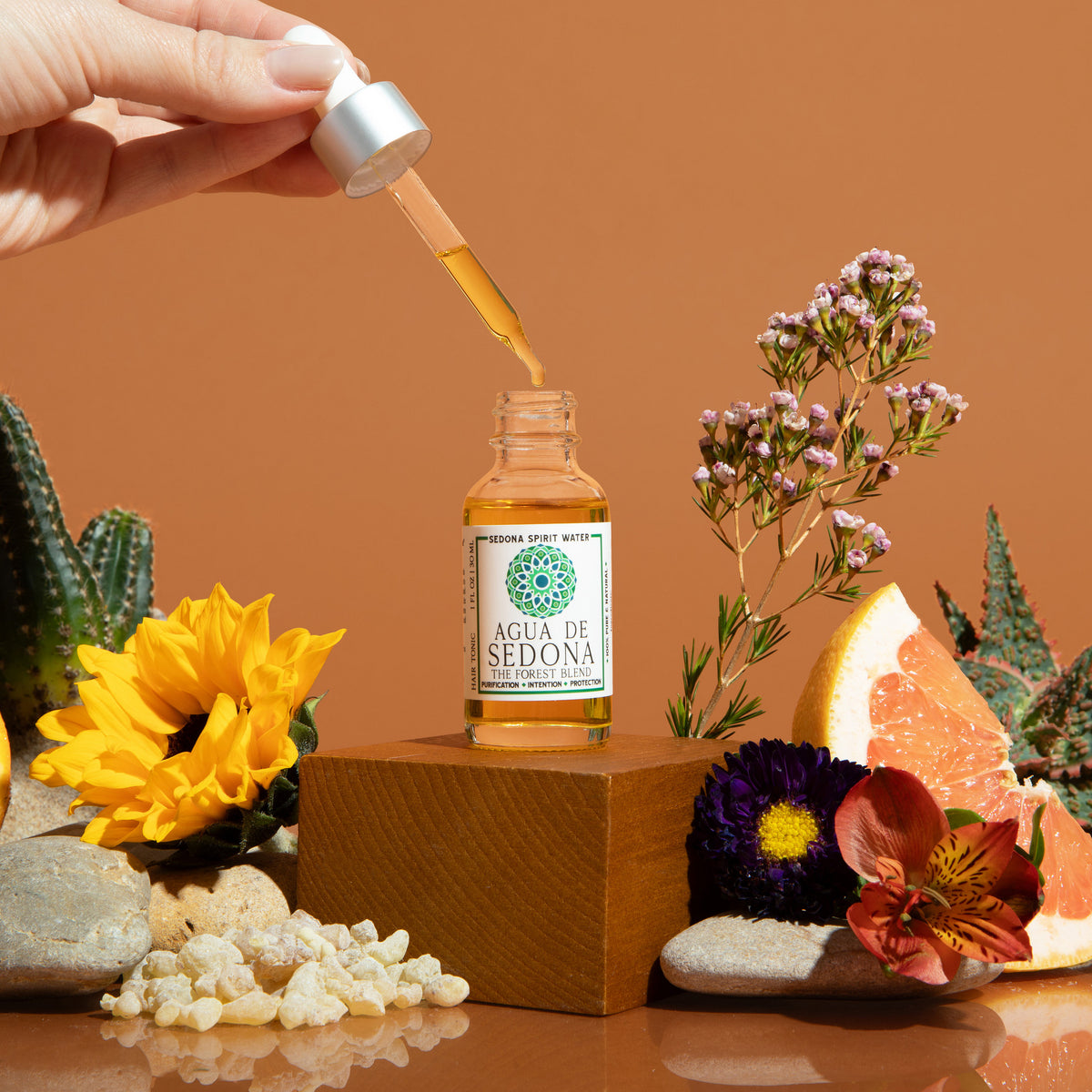 Agua de Sedona dropper bottle with flowers, grapefruit, and crystals on a warm brown backdrop