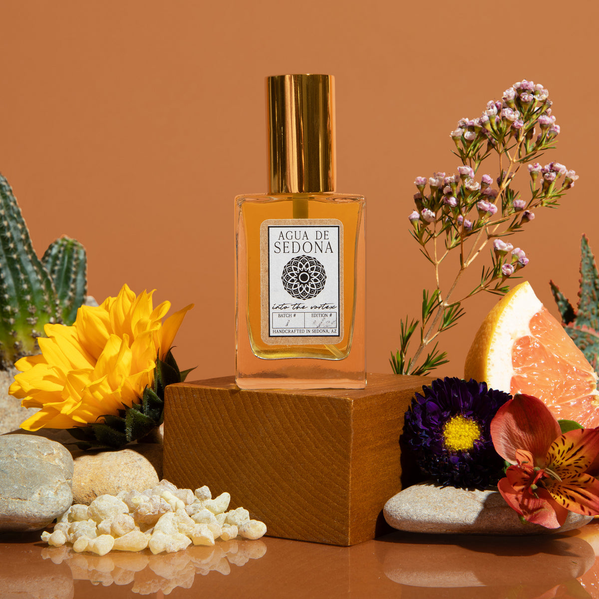 Agua de Sedona perfume bottle with golden cap surrounded by flowers, citrus, and desert elements.