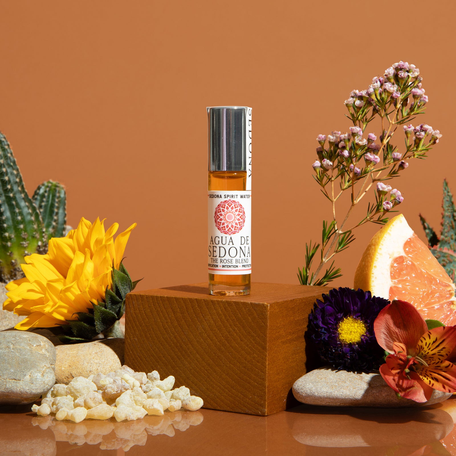 Agua de Sedona Rose Blend roll-on perfume with citrus fruits, lavender, and colorful florals on the background
