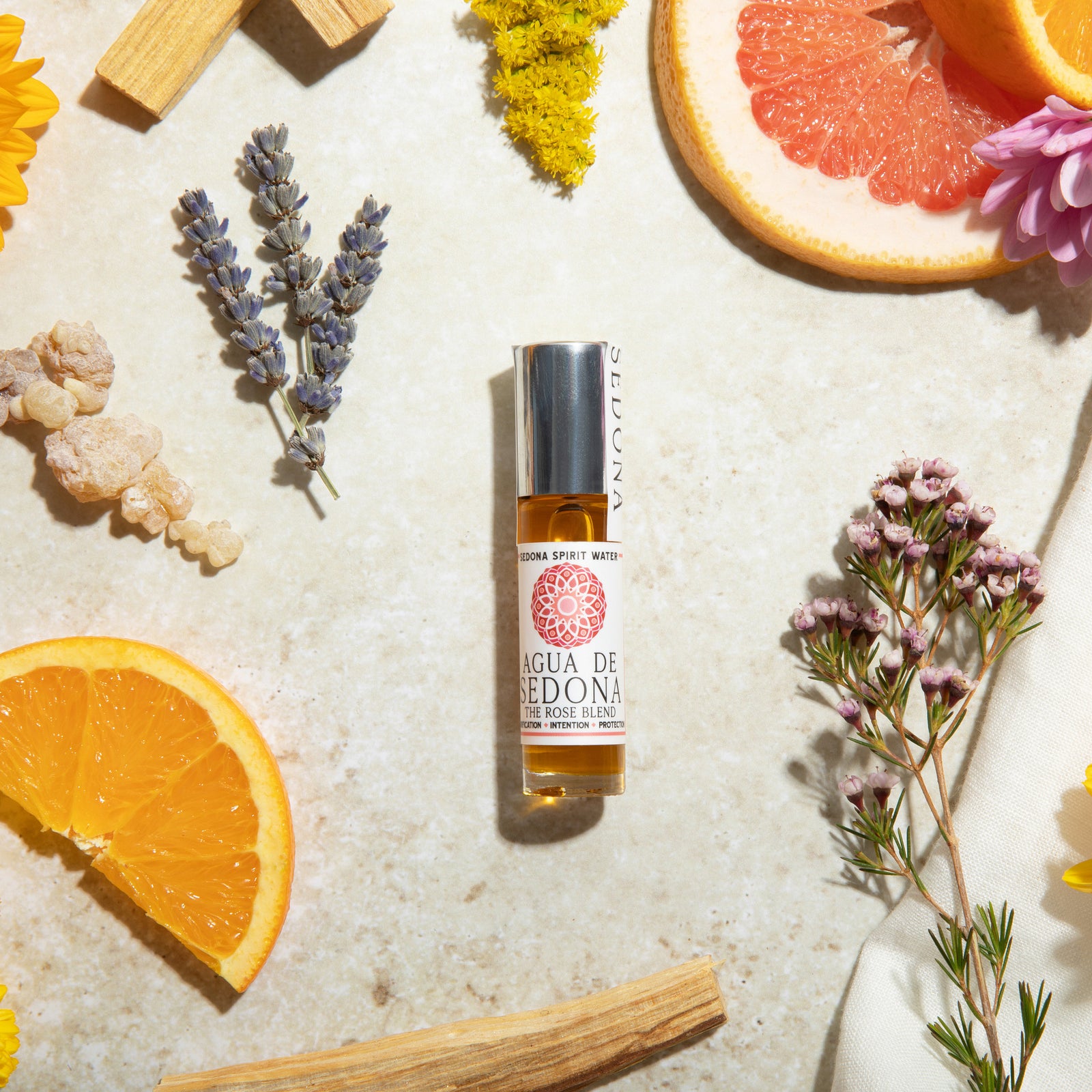 Agua de Sedona Rose Blend roll-on perfume with citrus fruits, lavender, and colorful florals on the background
