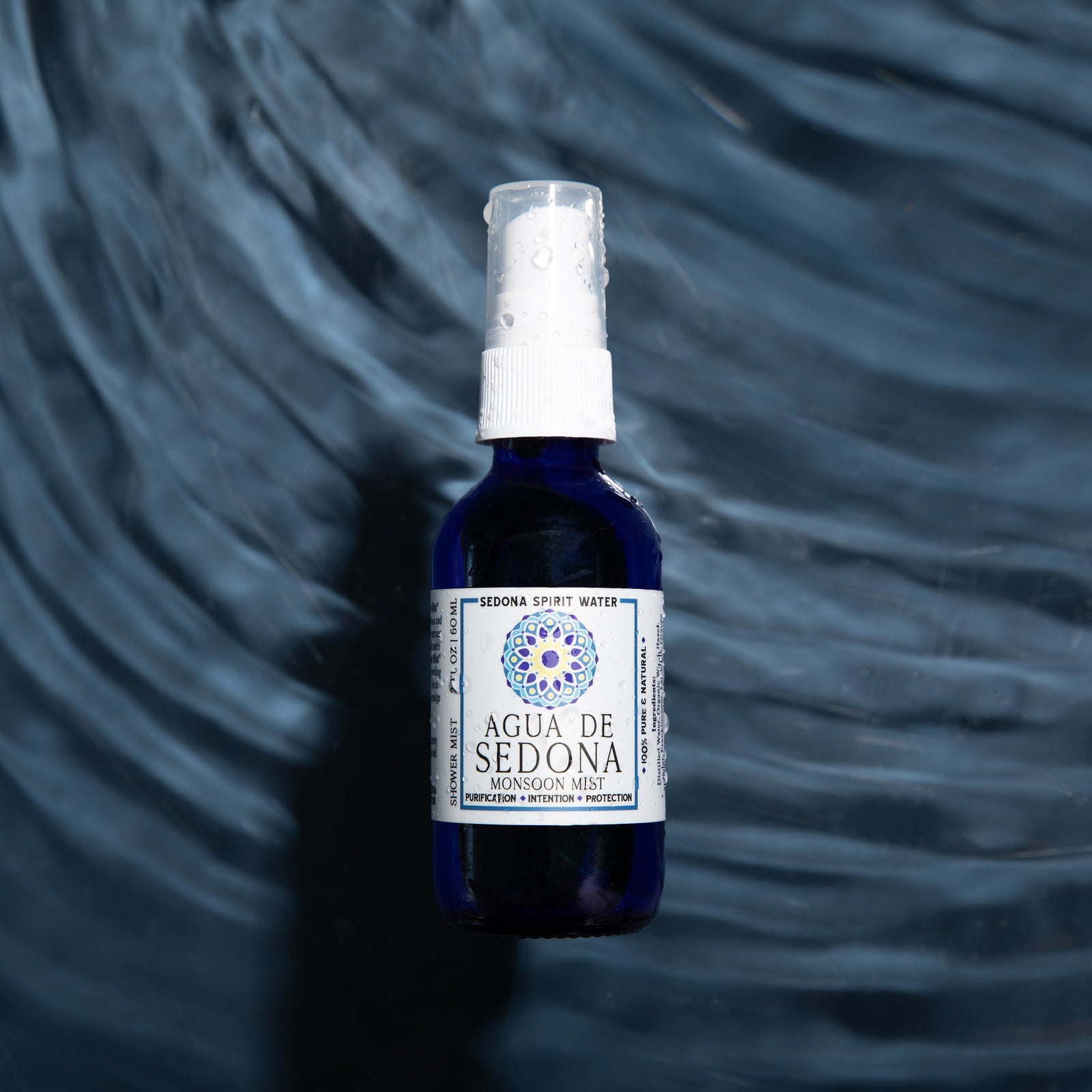 Agua de Sedona Monsoon Mist spray bottle on dark swirling water background for hydration and clarity.