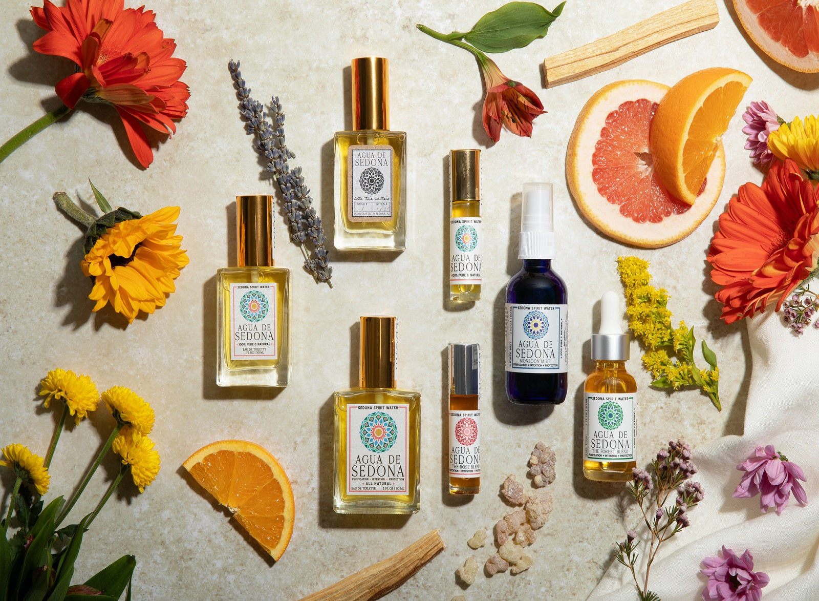 Agua de Sedona product collection with flowers, fruits, crystals, and natural elements on beige surface.