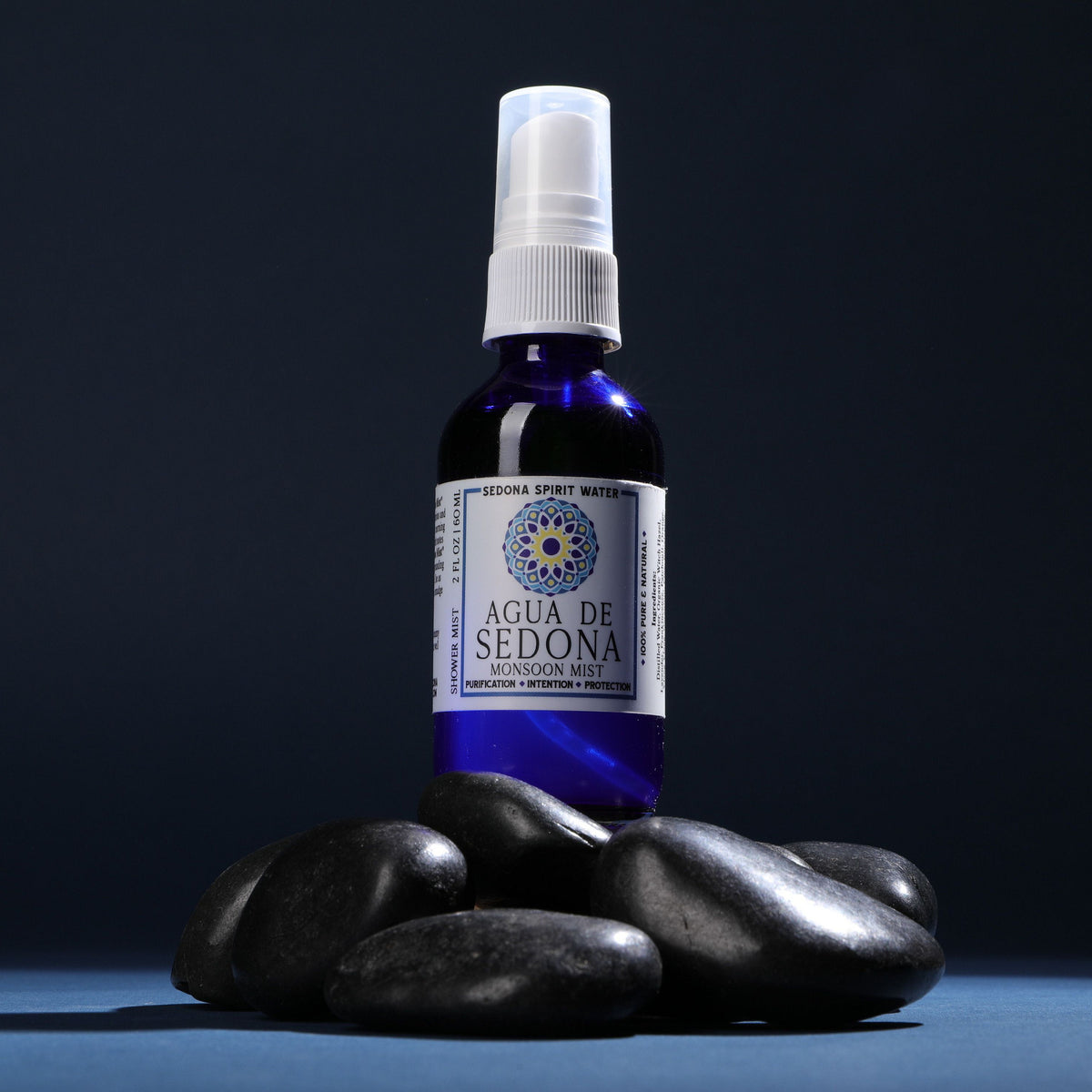 Agua de Sedona - monsoon mist. blue perfume bottle on top of black lava rocks with blue background